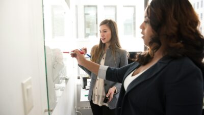 two women writing on glass panel