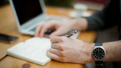 man sitting while writing on notebook